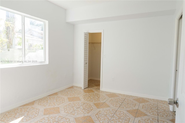 unfurnished bedroom with light tile patterned floors, a closet, baseboards, and a walk in closet
