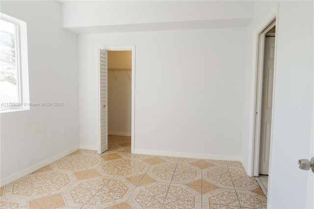 unfurnished bedroom with light tile patterned floors, a spacious closet, a closet, and baseboards