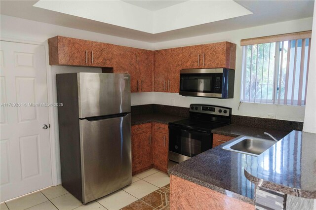 kitchen with a sink, brown cabinets, appliances with stainless steel finishes, and light tile patterned floors