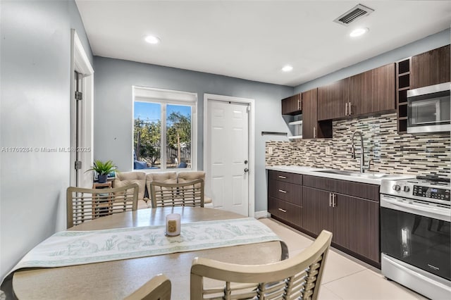 kitchen with stainless steel appliances, dark brown cabinetry, a sink, open shelves, and backsplash