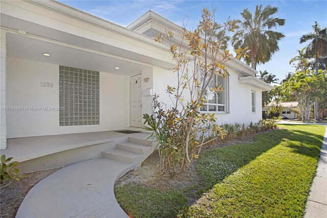 view of exterior entry featuring stucco siding, covered porch, and a yard