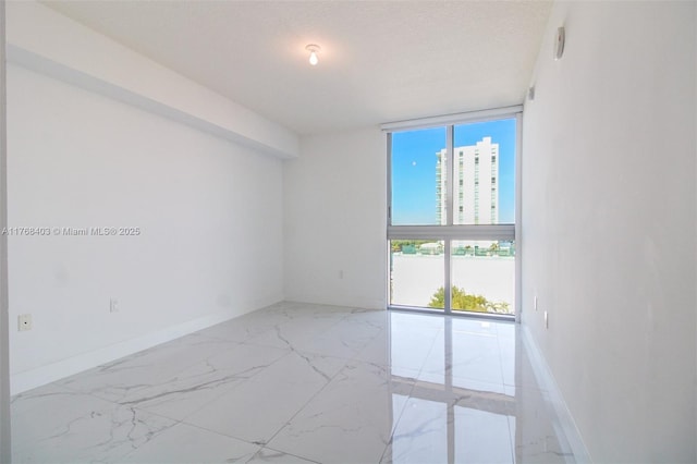 unfurnished room with expansive windows, a textured ceiling, marble finish floor, and baseboards