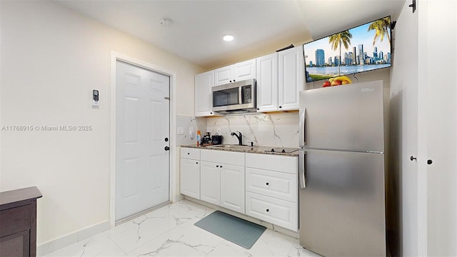 kitchen with a sink, backsplash, white cabinetry, appliances with stainless steel finishes, and marble finish floor
