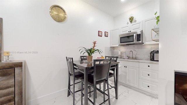 kitchen featuring a sink, stainless steel microwave, marble finish floor, white cabinets, and decorative backsplash