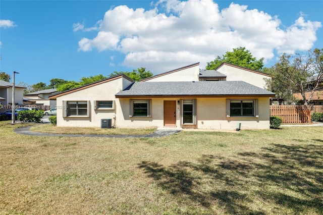 rear view of house with fence, stucco siding, roof with shingles, a lawn, and cooling unit