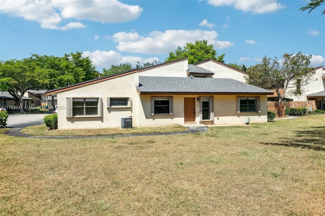view of front of house featuring a front lawn, central air condition unit, stucco siding, and fence