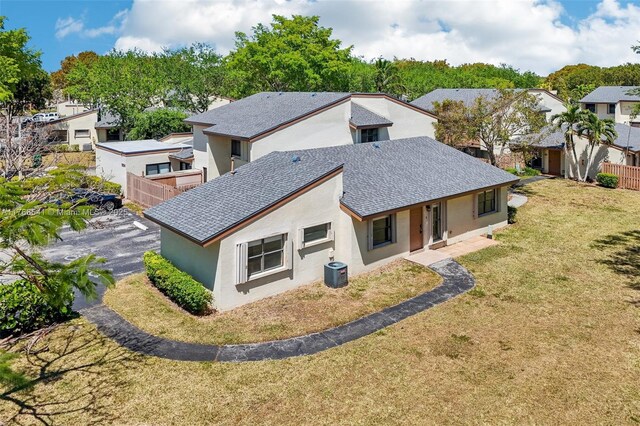 rear view of house featuring central AC unit, a lawn, stucco siding, and fence