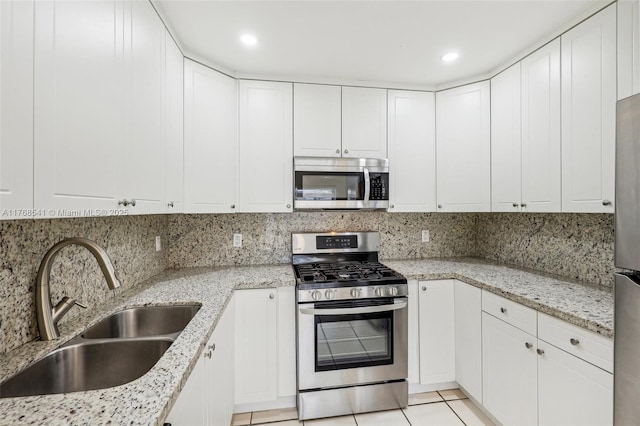 kitchen featuring white cabinetry, light tile patterned floors, backsplash, a sink, and appliances with stainless steel finishes