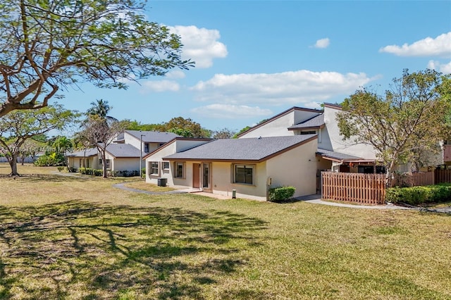 back of property with stucco siding, fence, and a lawn