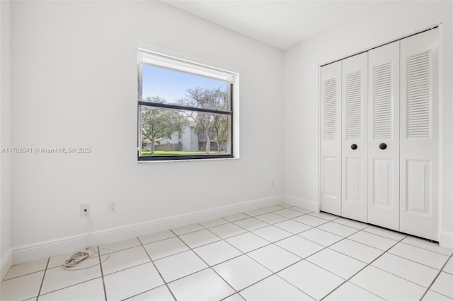 unfurnished bedroom with a closet, baseboards, and light tile patterned floors