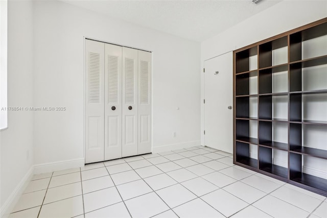 unfurnished bedroom with baseboards, a closet, a textured ceiling, and light tile patterned floors