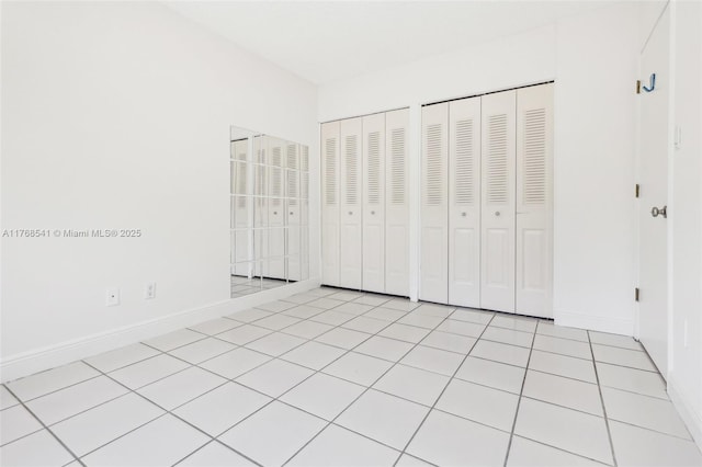 unfurnished bedroom featuring two closets, light tile patterned floors, and baseboards