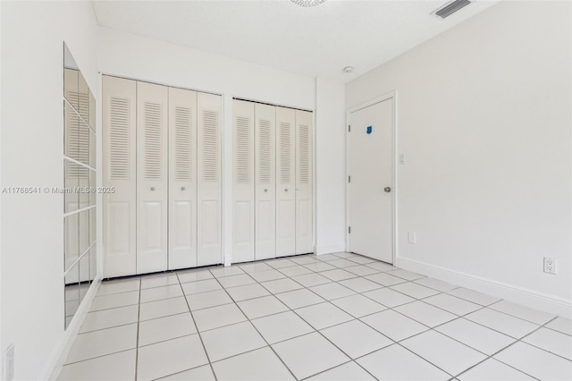 unfurnished bedroom featuring baseboards, visible vents, and two closets