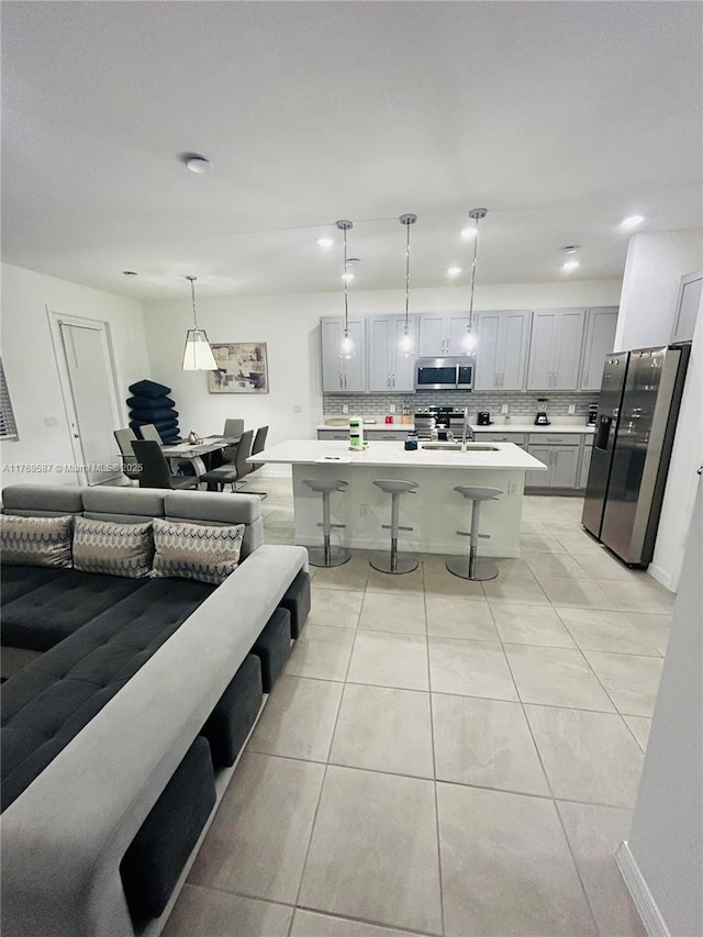 kitchen with a kitchen breakfast bar, light countertops, open floor plan, a sink, and appliances with stainless steel finishes