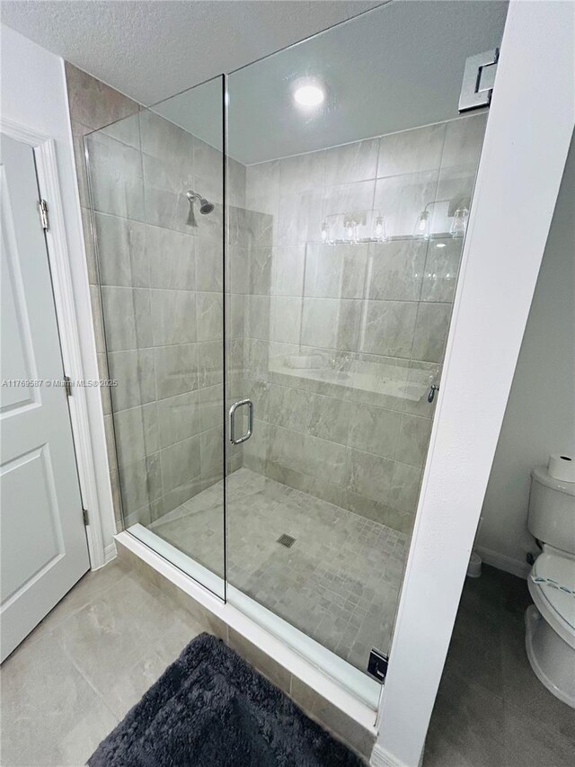full bath with a textured ceiling, toilet, and a stall shower