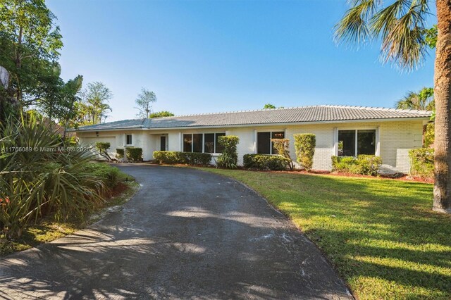 ranch-style home with a tile roof, aphalt driveway, a front lawn, brick siding, and a garage