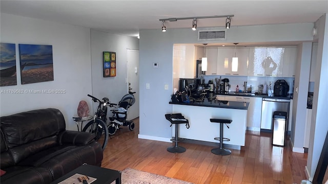 kitchen featuring white cabinets, a kitchen breakfast bar, dark countertops, visible vents, and dishwasher