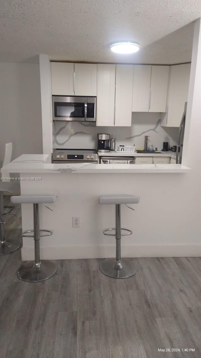 4630 NW 102nd Ave Unit 103-15, Doral, FL 33178 - kitchen featuring white cabinets, wood finished floors, a breakfast bar area, and appliances with stainless steel finishes