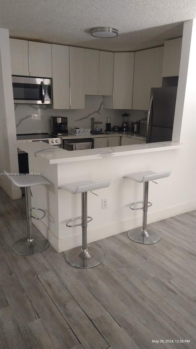 4630 NW 102nd Ave Unit 103-15, Doral, FL 33178 - kitchen featuring a textured ceiling, light wood-style flooring, a breakfast bar, stainless steel microwave, and freestanding refrigerator