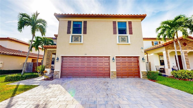 mediterranean / spanish-style home with stone siding, a tiled roof, decorative driveway, a garage, and stucco siding