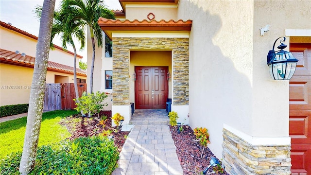 property entrance with stone siding, a tile roof, stucco siding, and fence
