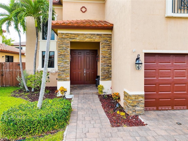 doorway to property with stone siding, fence, a tiled roof, and stucco siding