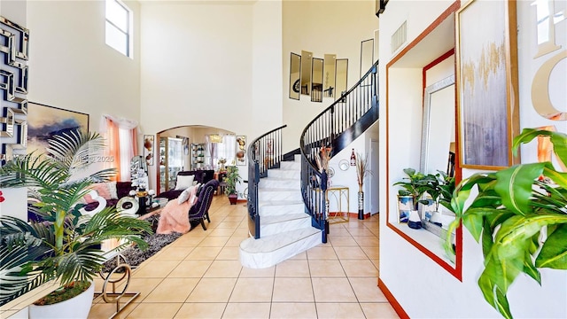 entrance foyer featuring stairway, light tile patterned floors, a towering ceiling, arched walkways, and visible vents