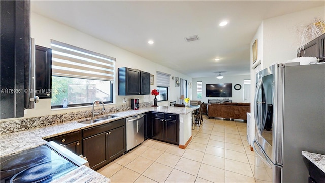kitchen featuring light stone counters, appliances with stainless steel finishes, a sink, open floor plan, and light tile patterned floors