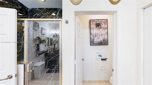 bathroom with toilet, a marble finish shower, and tile patterned floors