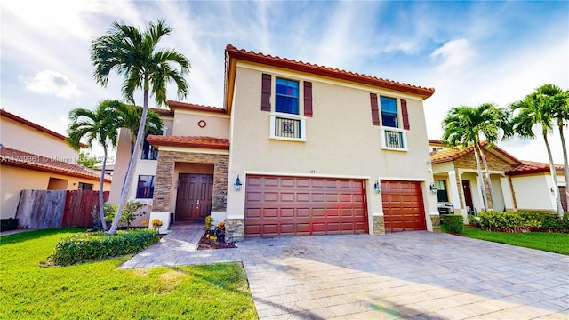 mediterranean / spanish home featuring stone siding, stucco siding, an attached garage, a tiled roof, and decorative driveway