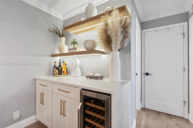 bar featuring light wood finished floors, a bar, baseboards, ornamental molding, and wine cooler