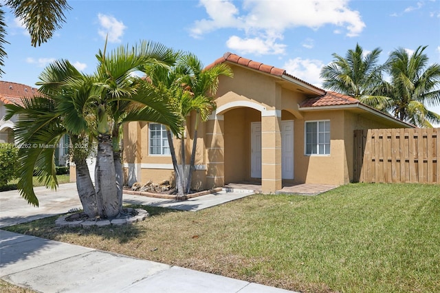 mediterranean / spanish home featuring a front lawn, a tile roof, stucco siding, and fence