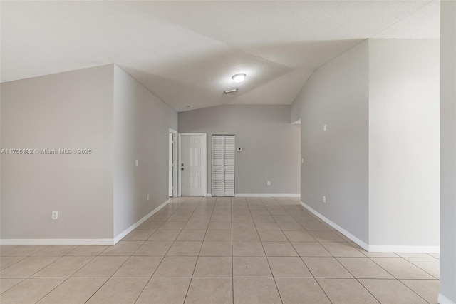 spare room featuring light tile patterned floors, baseboards, and lofted ceiling