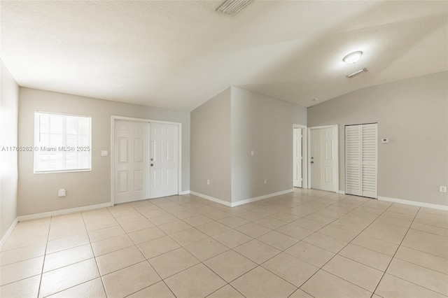 spare room featuring light tile patterned flooring, baseboards, lofted ceiling, and visible vents