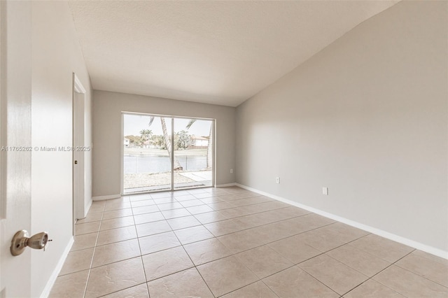 empty room featuring light tile patterned flooring, baseboards, and vaulted ceiling