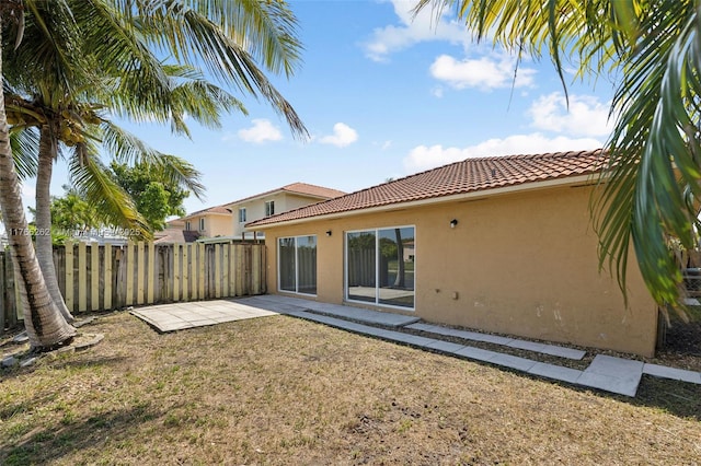 rear view of property featuring a tile roof, stucco siding, fence, and a patio