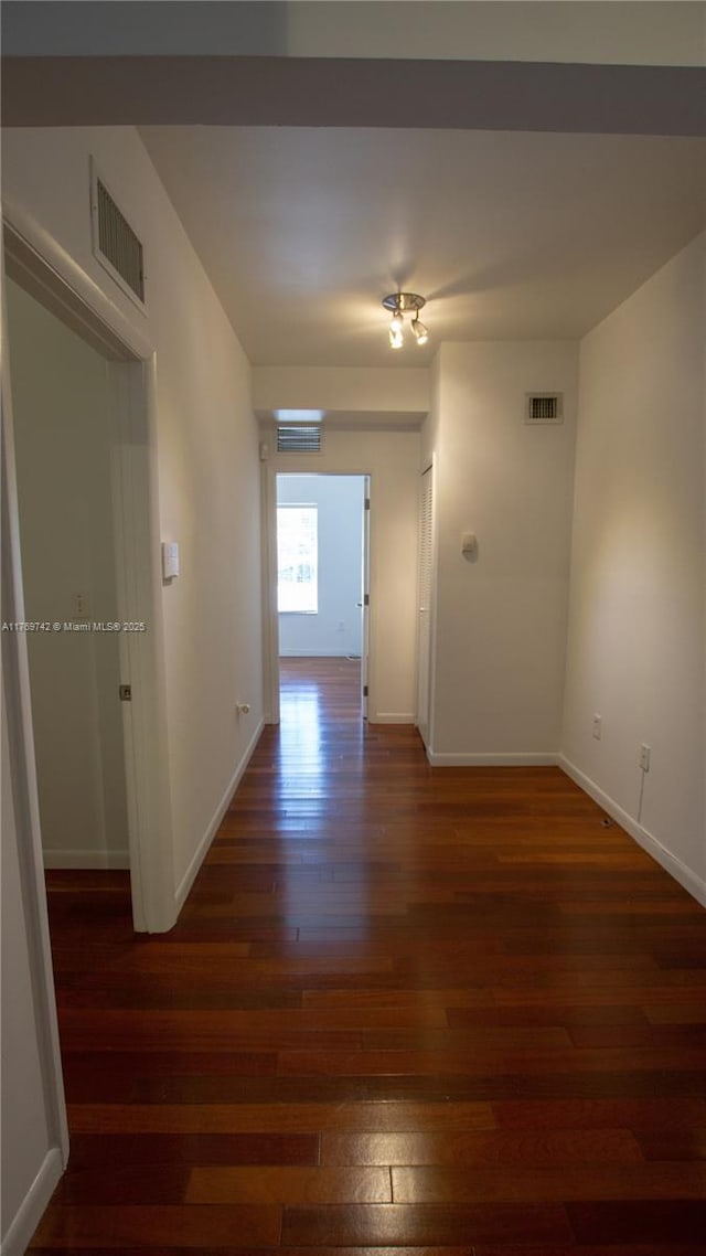 hall featuring baseboards, visible vents, and wood finished floors