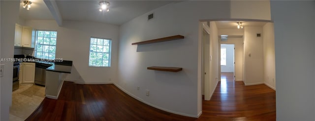 hallway featuring beam ceiling, wood finished floors, baseboards, visible vents, and arched walkways