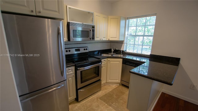 kitchen with white cabinets, a sink, a peninsula, and appliances with stainless steel finishes