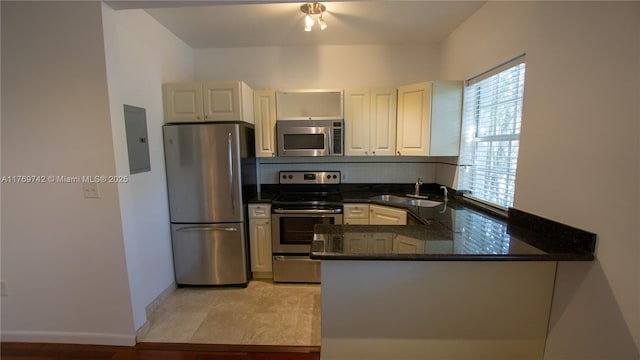 kitchen featuring stainless steel appliances, dark stone counters, a sink, a peninsula, and electric panel