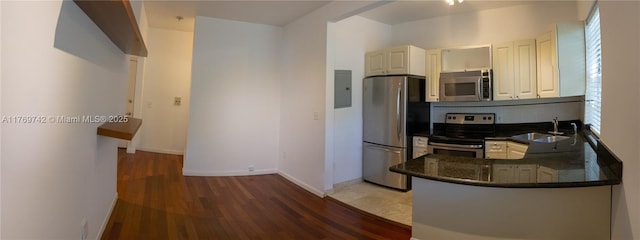 kitchen with stainless steel appliances, dark stone countertops, baseboards, a sink, and wood finished floors