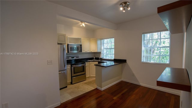 kitchen with light wood-type flooring, stainless steel appliances, baseboards, dark countertops, and a peninsula