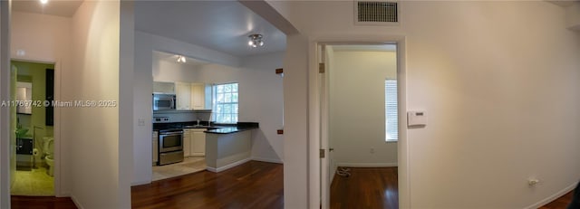 corridor featuring baseboards, dark wood-style floors, visible vents, and a sink