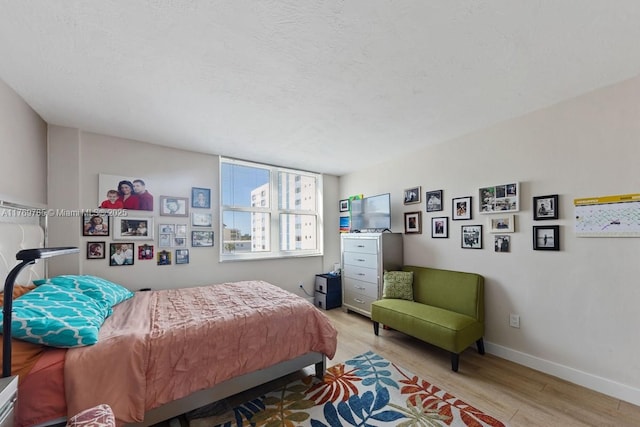 bedroom featuring baseboards, a textured ceiling, and light wood finished floors