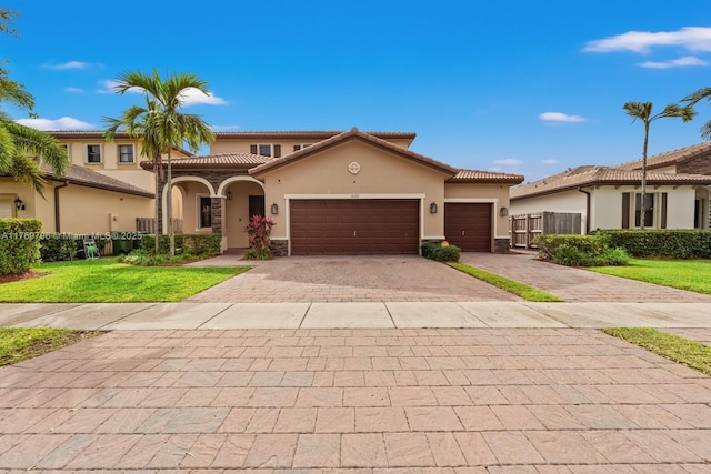mediterranean / spanish home featuring stucco siding, fence, decorative driveway, a garage, and a front yard