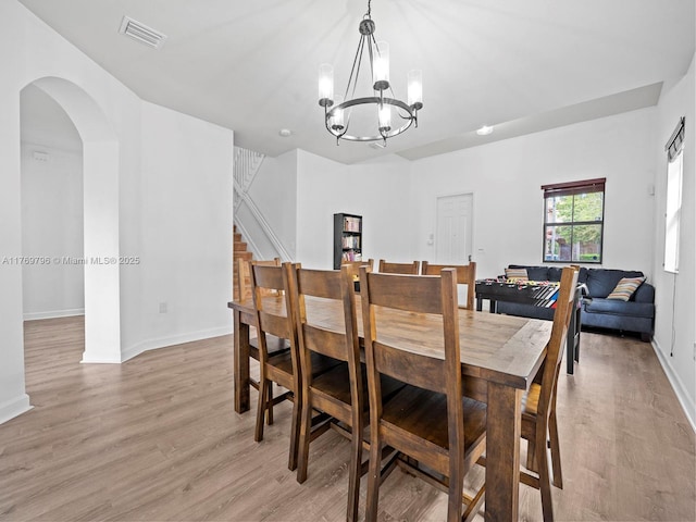 dining area with an inviting chandelier, light wood-style floors, visible vents, baseboards, and arched walkways