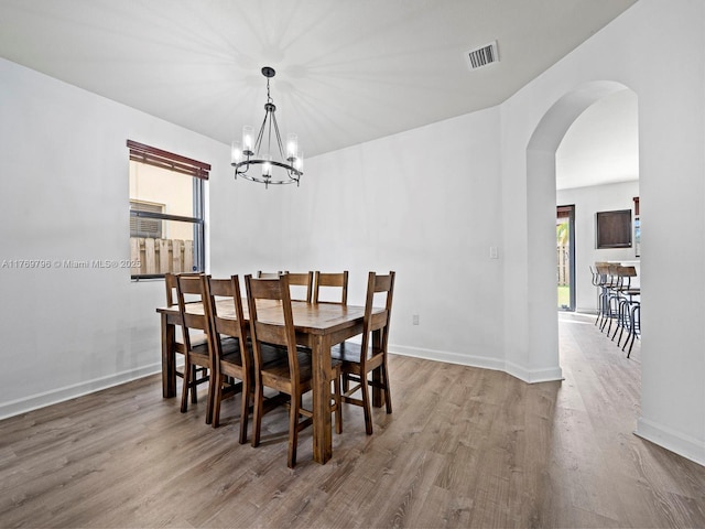 dining space featuring visible vents, a chandelier, baseboards, arched walkways, and wood finished floors