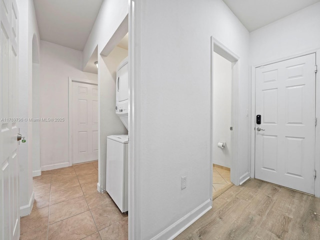 hallway with stacked washer and dryer, light tile patterned floors, and baseboards