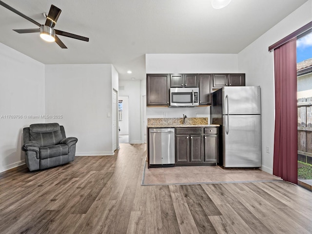 kitchen with appliances with stainless steel finishes, dark brown cabinetry, light wood finished floors, and a sink