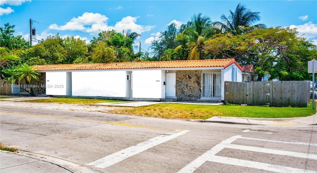 exterior space featuring a tiled roof, stucco siding, fence, and a front lawn